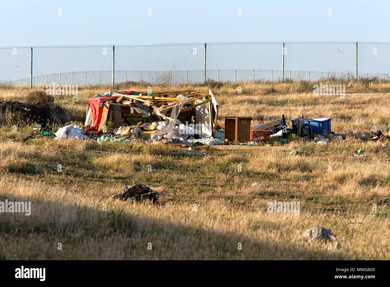 Homeless Camp against cyclone fence, dry grass, hillside. Stock Photo