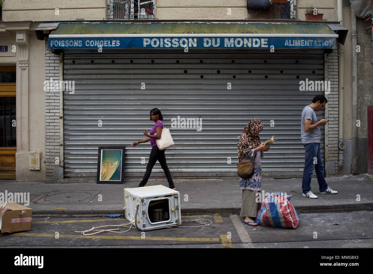 Woman in headscarf finds book among rubbish, Poisson du Monde, Rue de Suez, Goutte d'Or, Paris, France Stock Photo