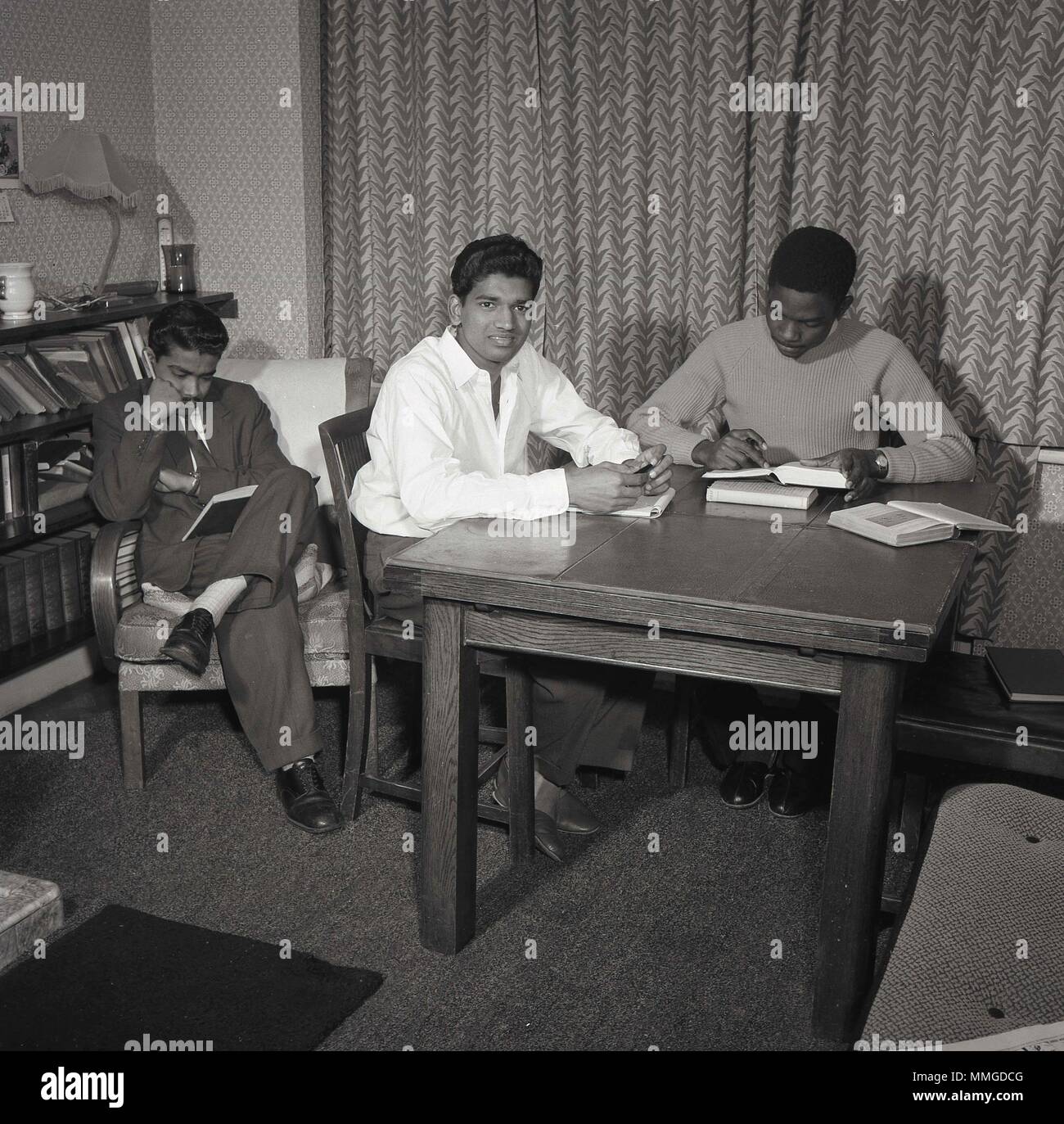 1950s, historical picture shows three male overseas students from the Commonwealth countries at their British lodgings studying, London, England, UK. Post-war Britain saw a big rise in the number of people from overseas coming to work, study and live in the country. Stock Photo