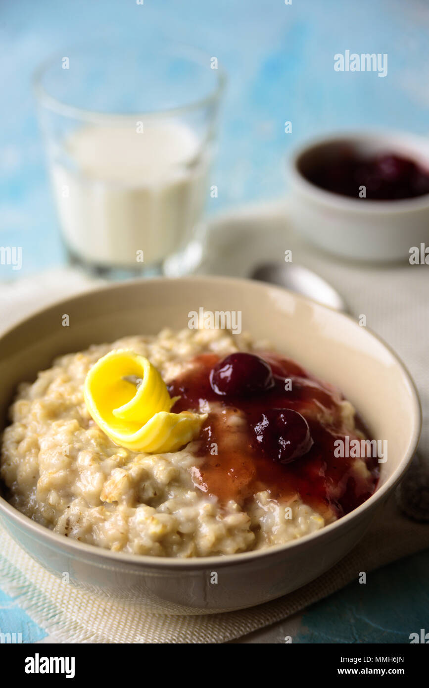 Oatmeal porrige with butter and cherry jam on blue table. With glass of milk. Breakfast Stock Photo
