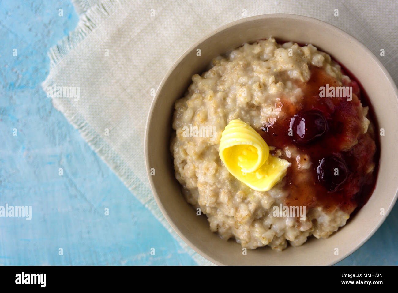 Oatmeal porrige with butter and cherry jam on blue table. With glass of milk. Breakfast Stock Photo
