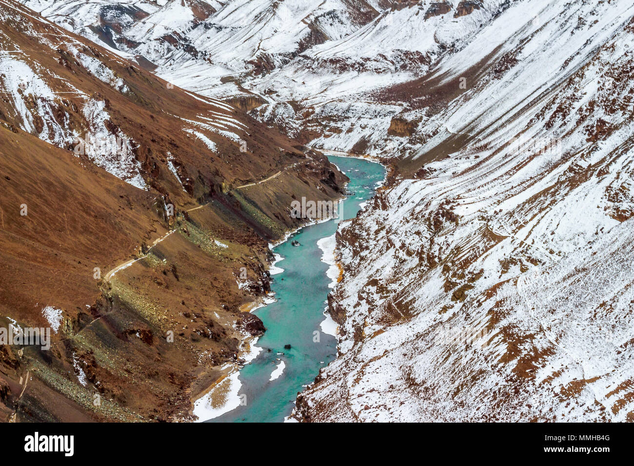 Indus river flowing through the snow capped mountains of Himalayas (Ladakh Range ) on one side and other side with a barren mountain. Stock Photo