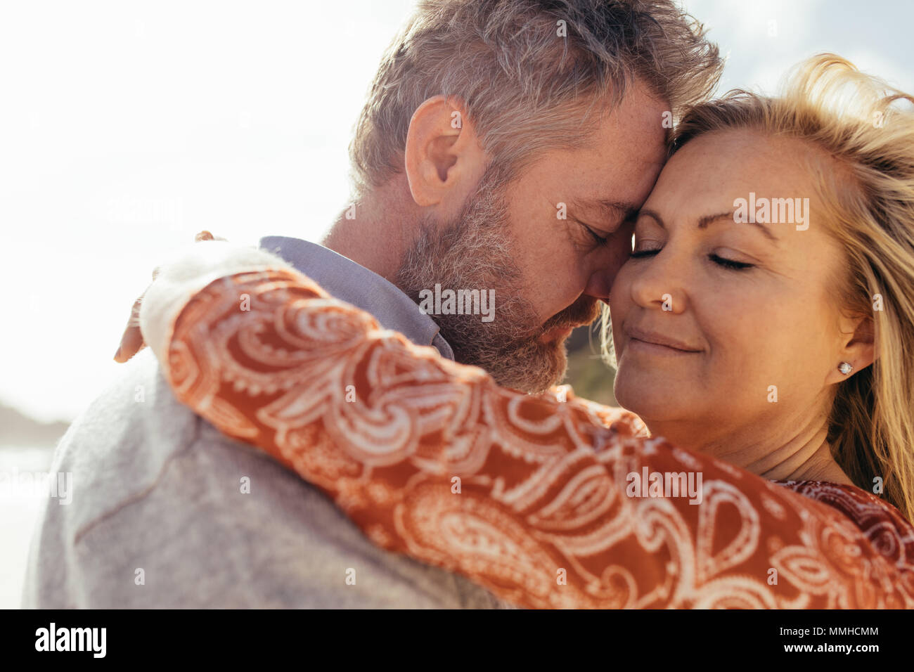 Affectionate senior couple embracing outdoors on beach. Beautiful mature woman being embraced by her loving husband on the beach. Stock Photo