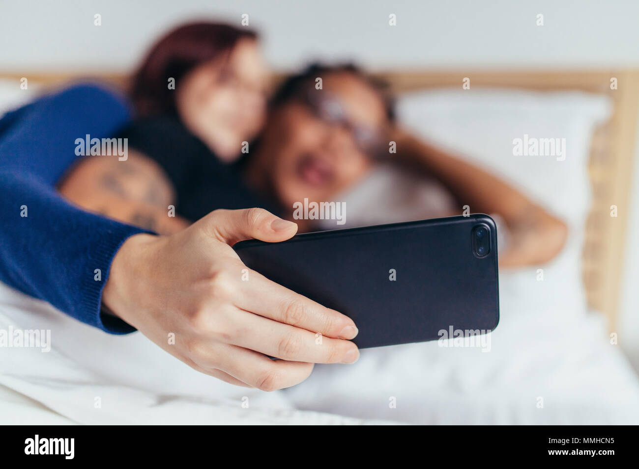Couple lying together on bed and taking selfie with smart phone. Focus on mobile phone in hand of woman. Stock Photo