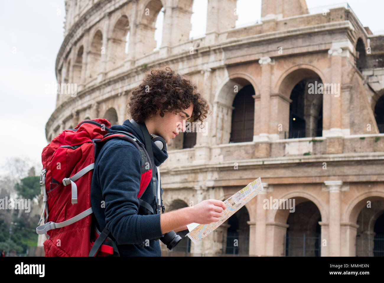 Handsome young traveler looking at tourist map in Rome in front of Colosseum. Backpacker with camera and tourist map Stock Photo