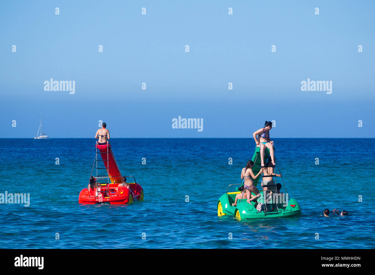 Young women riding colourful pedalos in the Mediterranean sea on a warm summer's day in Cala San Vicente, Mallorca, Spain. Stock Photo
