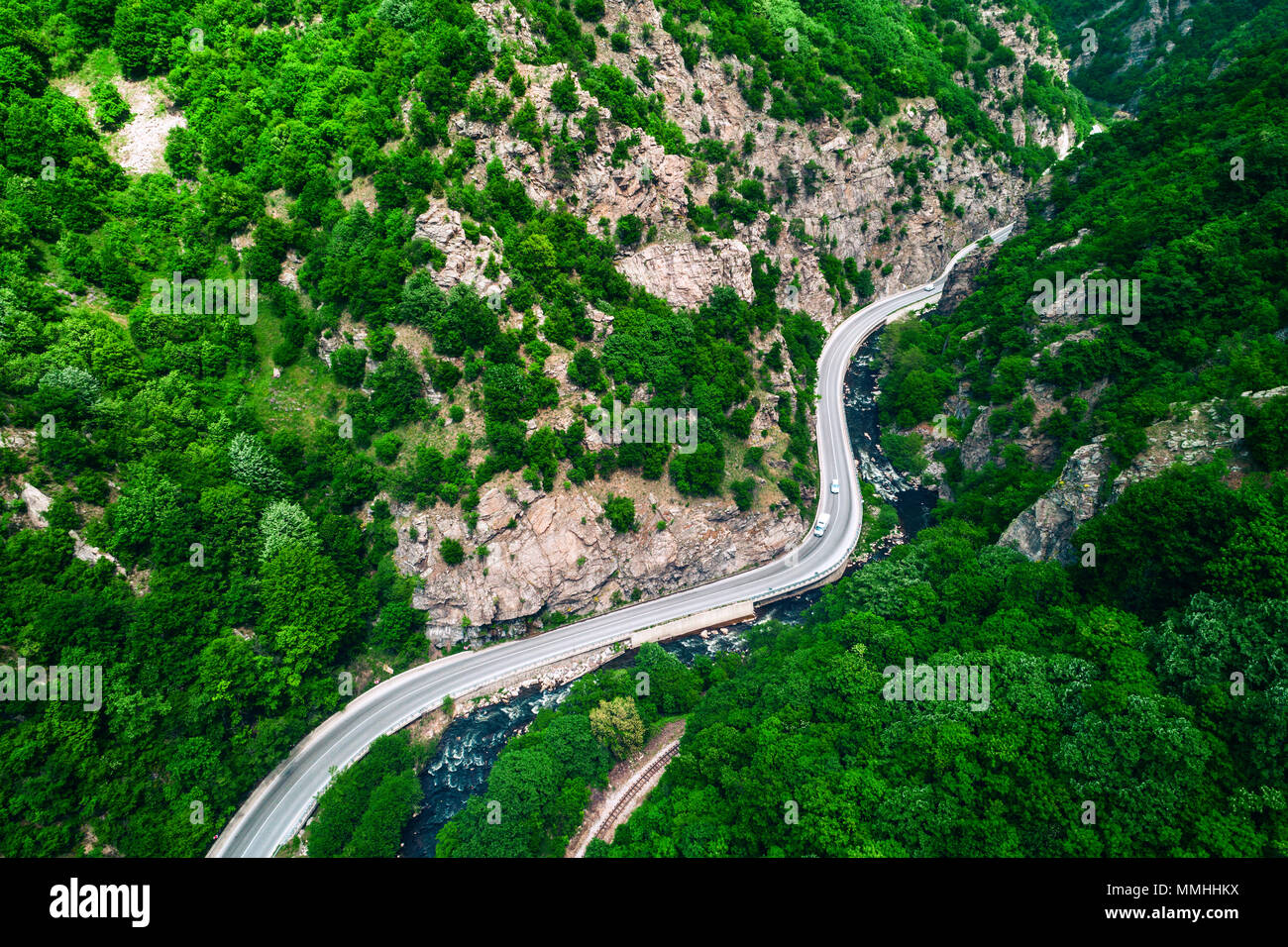 Aerial view of drone over mountain road and curves going through forest landscape Stock Photo