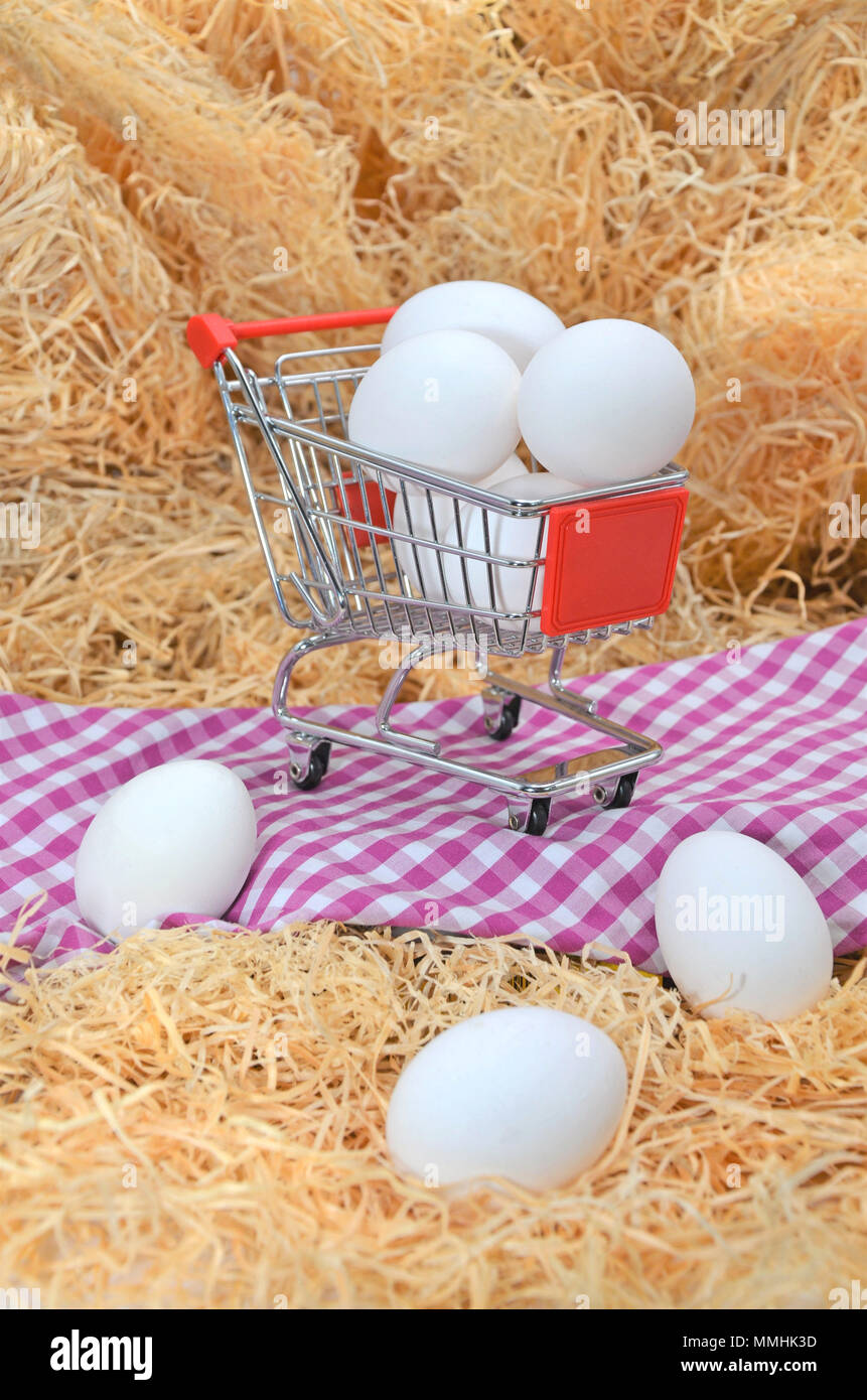 Eggs in shopping cart on a checkered tablecloth with straw Stock Photo