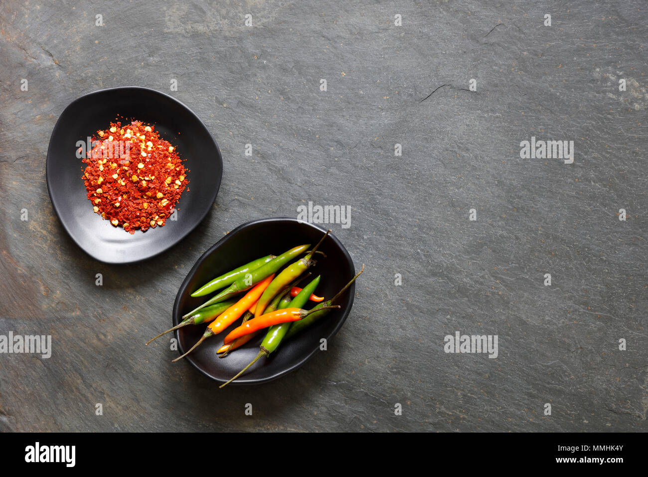 Ground dried chilli peppers with fresh peppers in black bowls with copy space Stock Photo