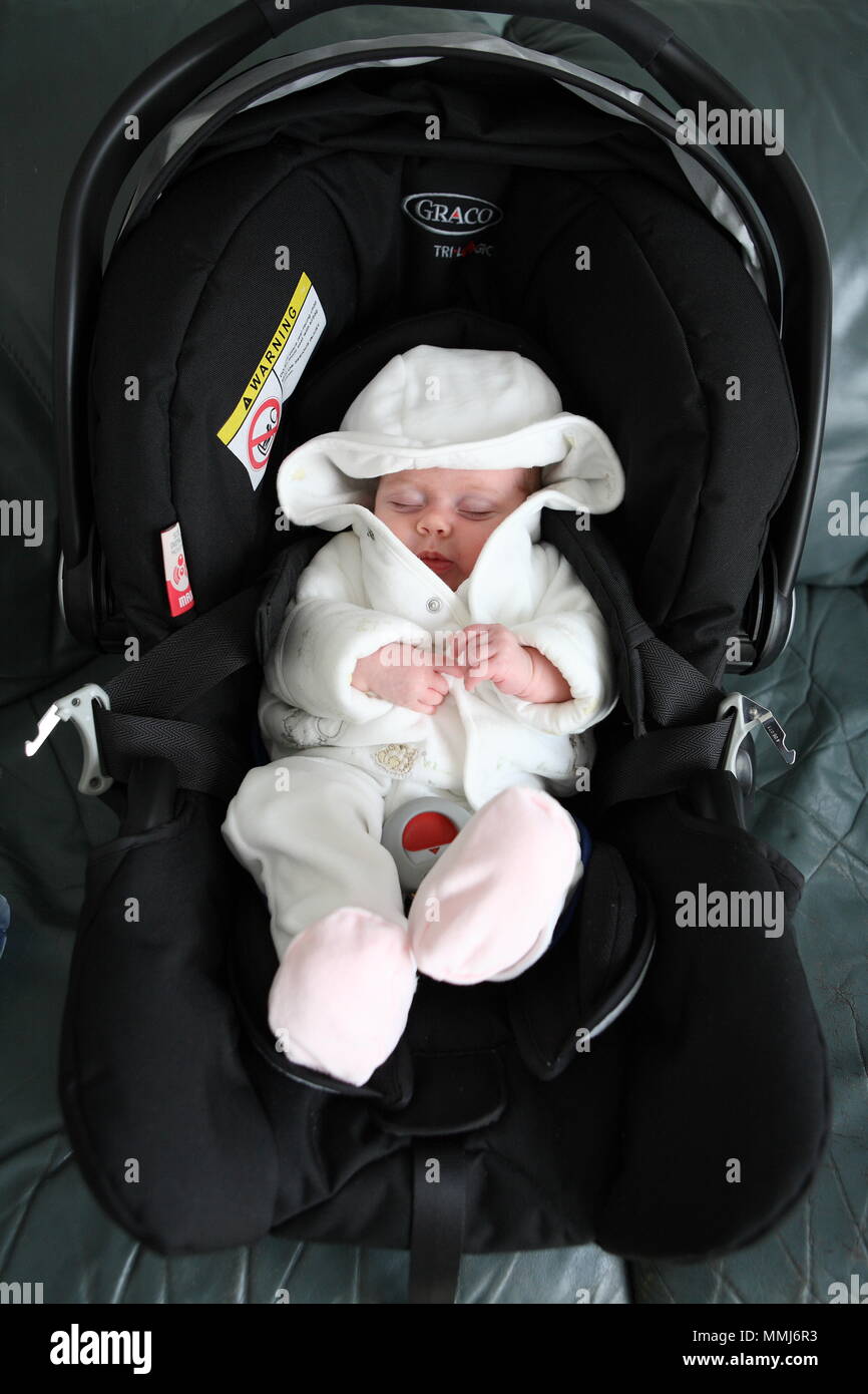 A new born baby in cute whit baby suit sits in a car seat ready to go