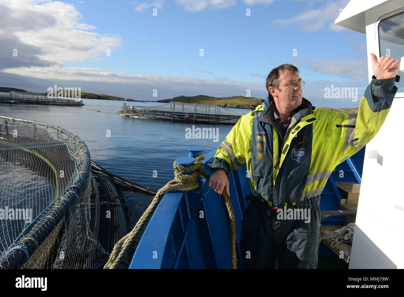 Salmon farmer on a salmon boat tying it up to cages before feeding the fish in the cages Stock Photo