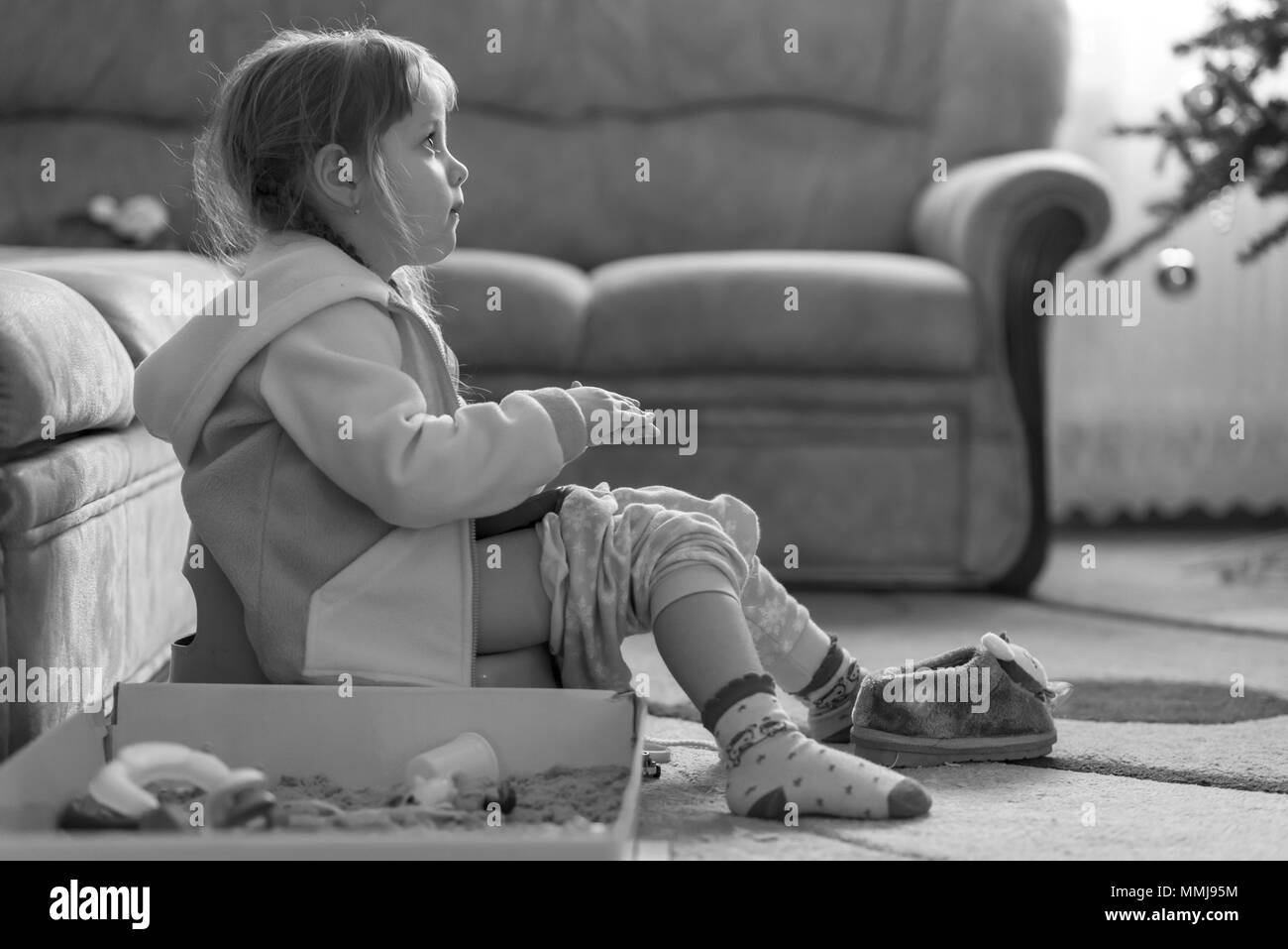 Little four years old girl sitting on potty, playing with kinetic sand and watching TV, monochrome effect Stock Photo