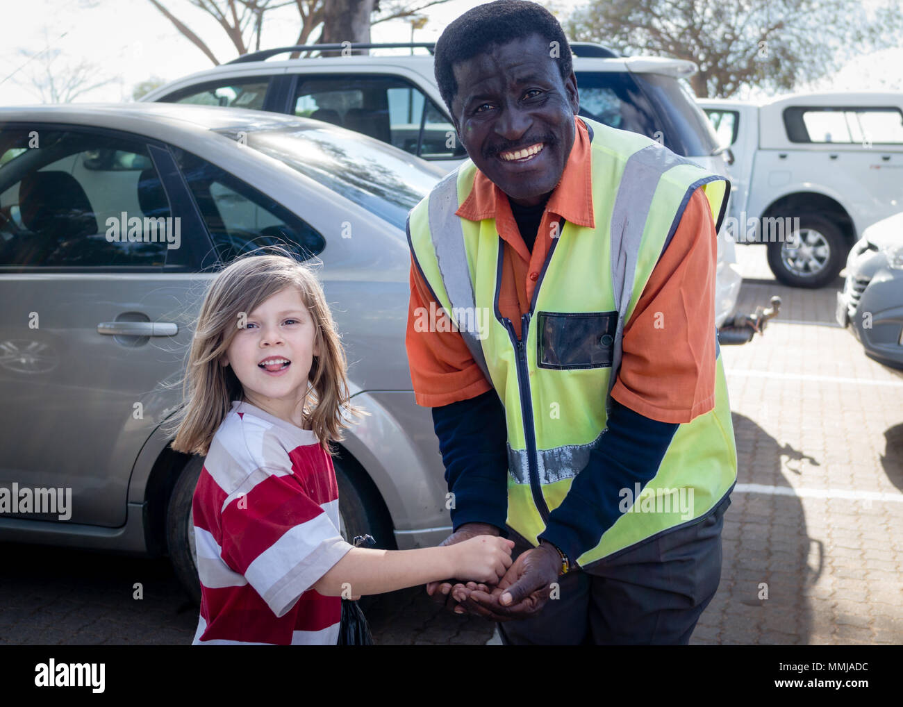 Young Caucasian White Girl Tipping Friendly Black South African Security Guard / Attendant in Outside Car Park - Controversial Self-Employment Stock Photo