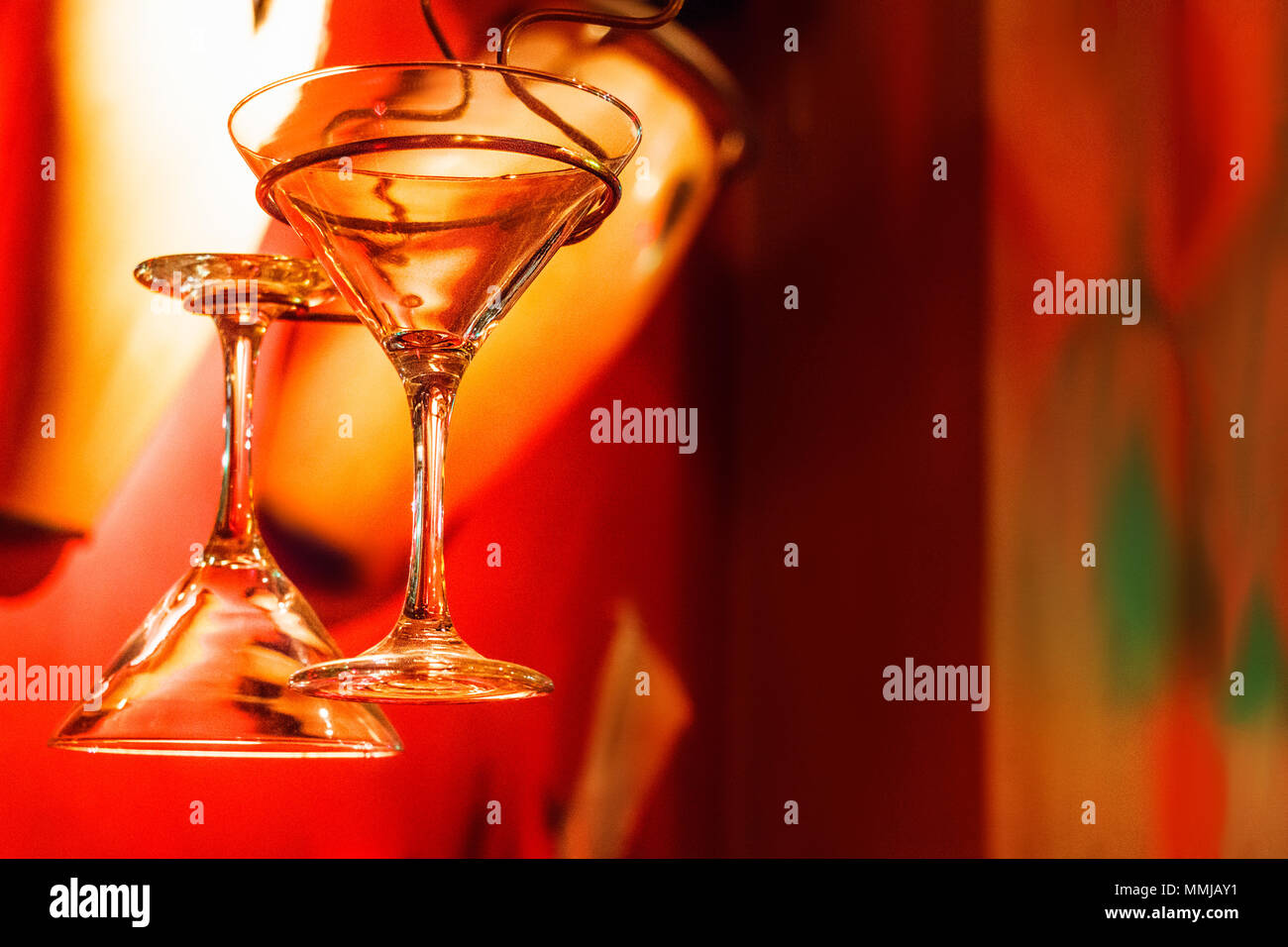 Two martini glasses hanging with a strong red color background Stock