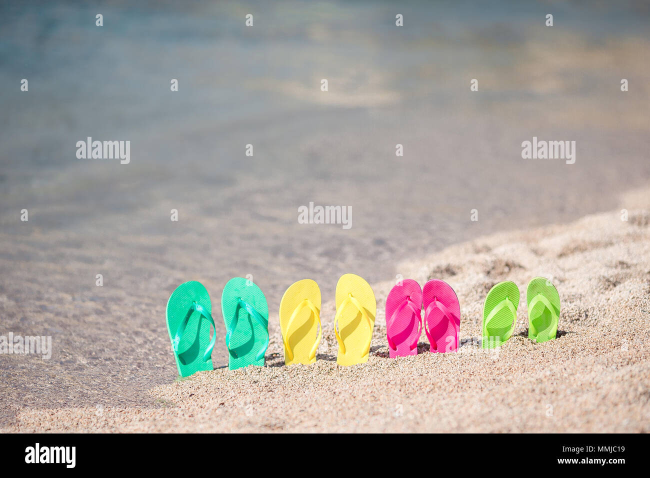 Family flip flops on beach in front of the blue sea. Four flip flops in ...