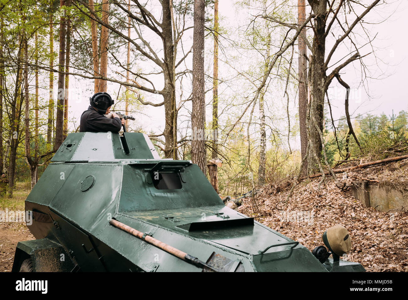 Re-enactor Dressed As Russian Soviet Crew Member Soldier Of World War II Sitting In Armoured Soviet Scout Car BA-64 In Forest And Aiming a Sub-machine Stock Photo