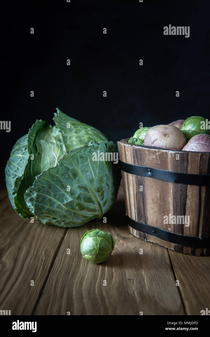 Selection of fresh garden vegetables (white cabbage, Brussels sprouts and pink potato tubers) on natural wooden background. Selective focus. Rustic st Stock Photo