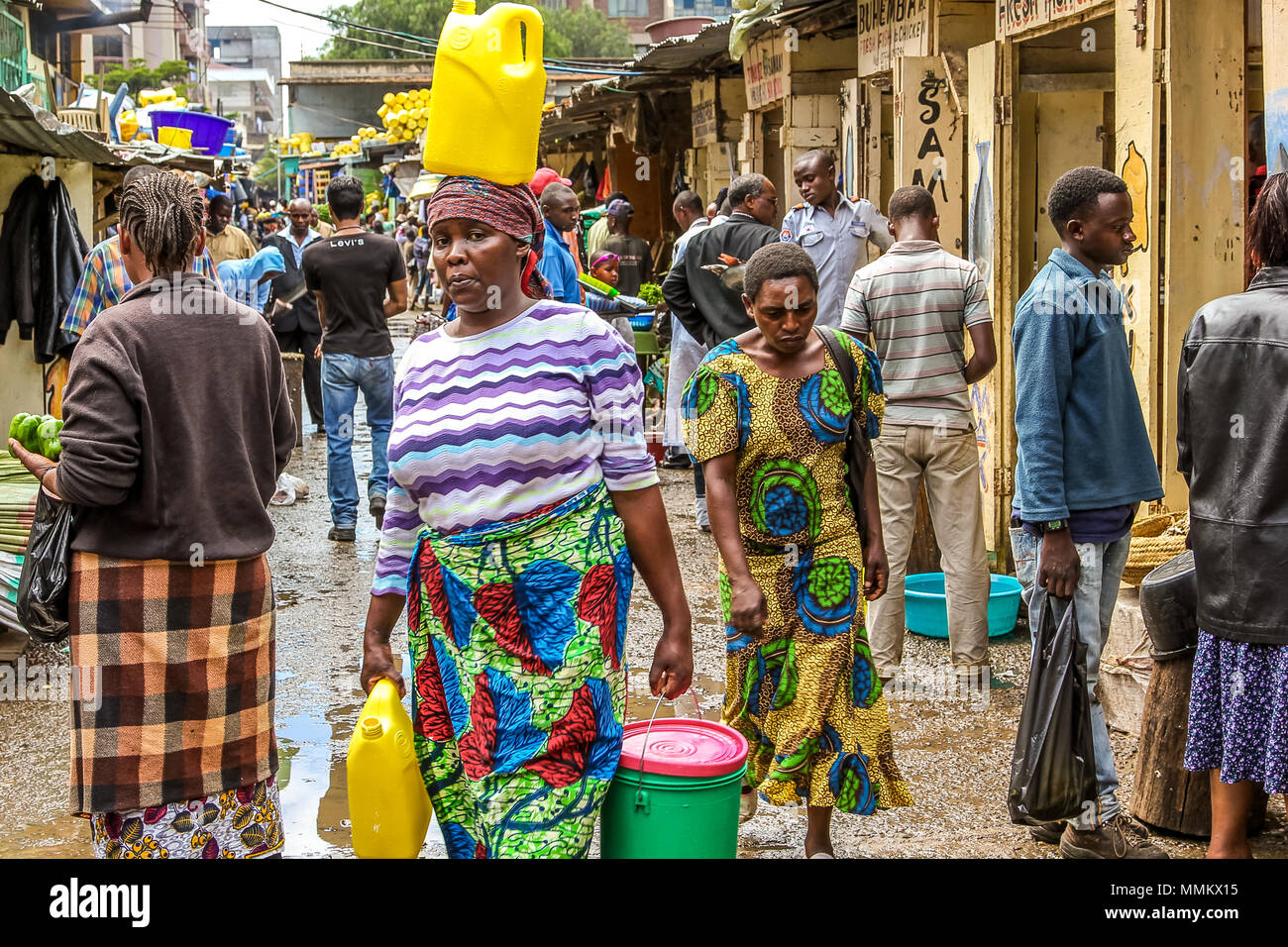 Arusha, Tanzania - January 2, 2013: A woman walks on her head carrying a yellow tank  in a market of the town Stock Photo