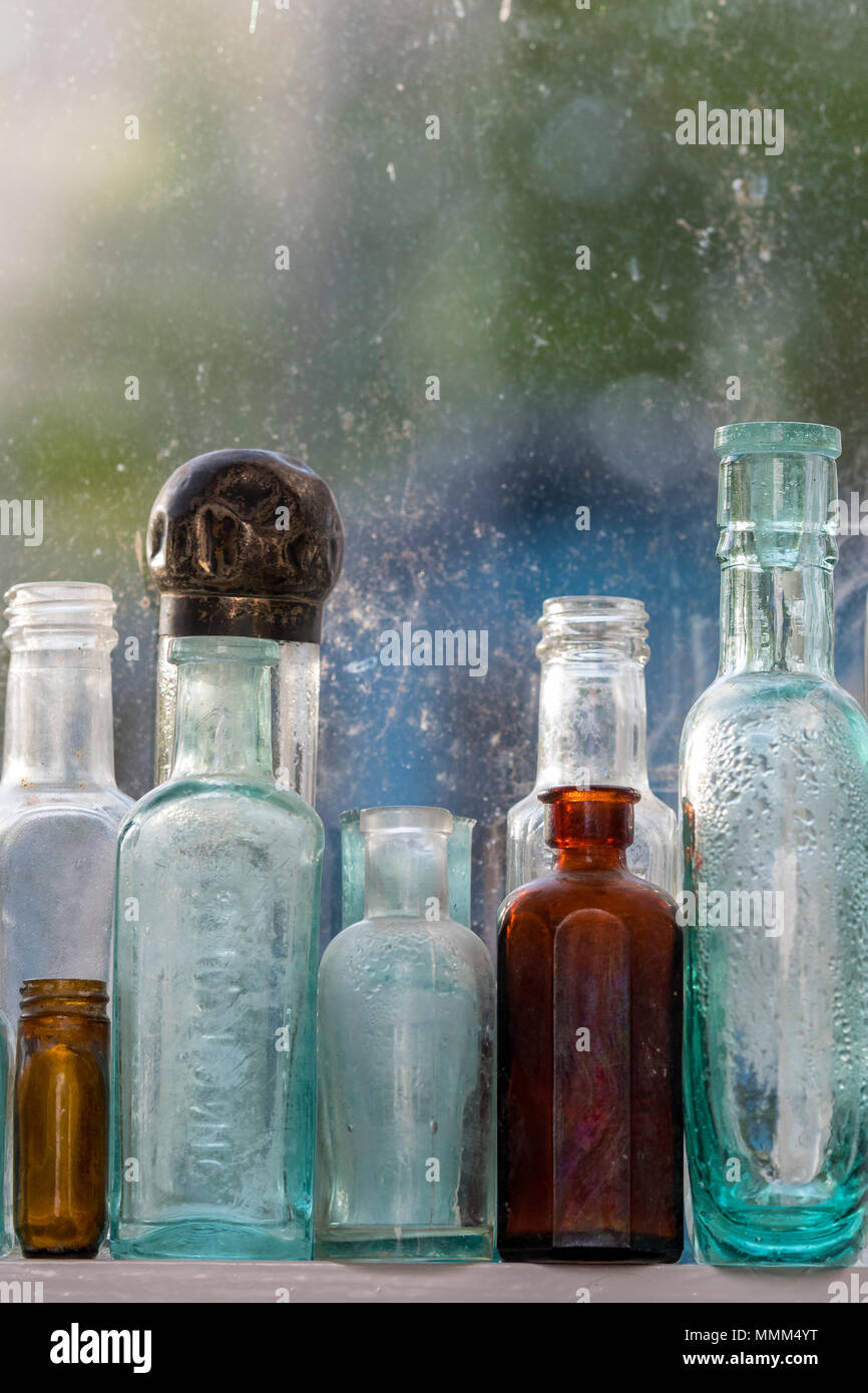 dusty old antique glass bottles on a window sill. vintage advertising glass medicine bottles. Stock Photo