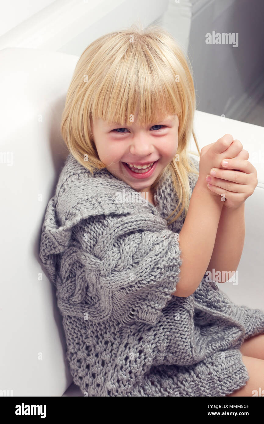 Girl 3 Years Old In A Gray Knit Sweater Sitting On A Sofa Girl 3 Years Old In A Gray Knit Sweater Sitting On A Sofa