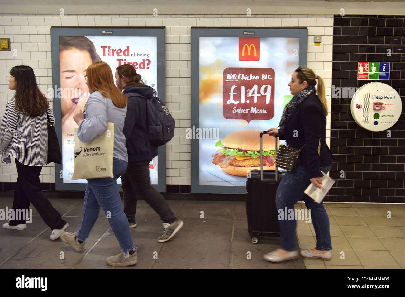 People walk past advertising hoardings promoting McDonalds BBQ Chicken burger in the Notting Hill underground station in central London.  Junk food ad Stock Photo