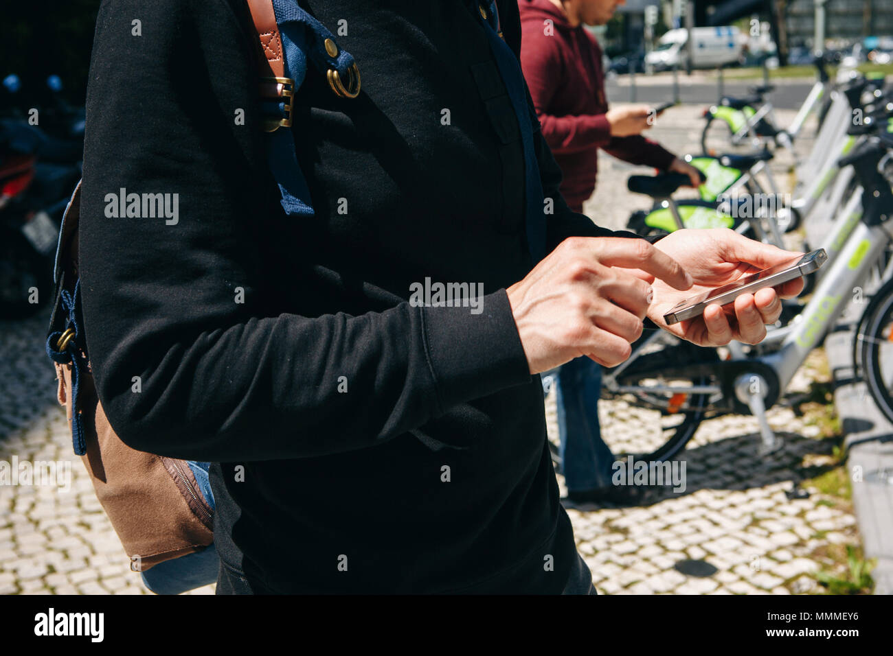 A male tourist hires a bicycle or an alternative environmental mode of transport using a mobile application on his phone. Or he simply dials a number and calls or uses the Internet on the street. Stock Photo