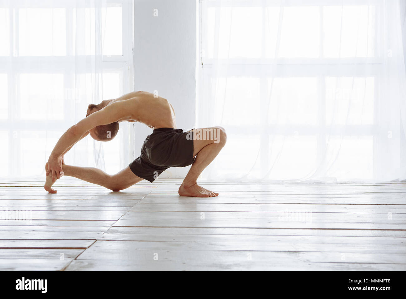 Fit muscular flexible man posing in difficult yoga pose Stock Photo