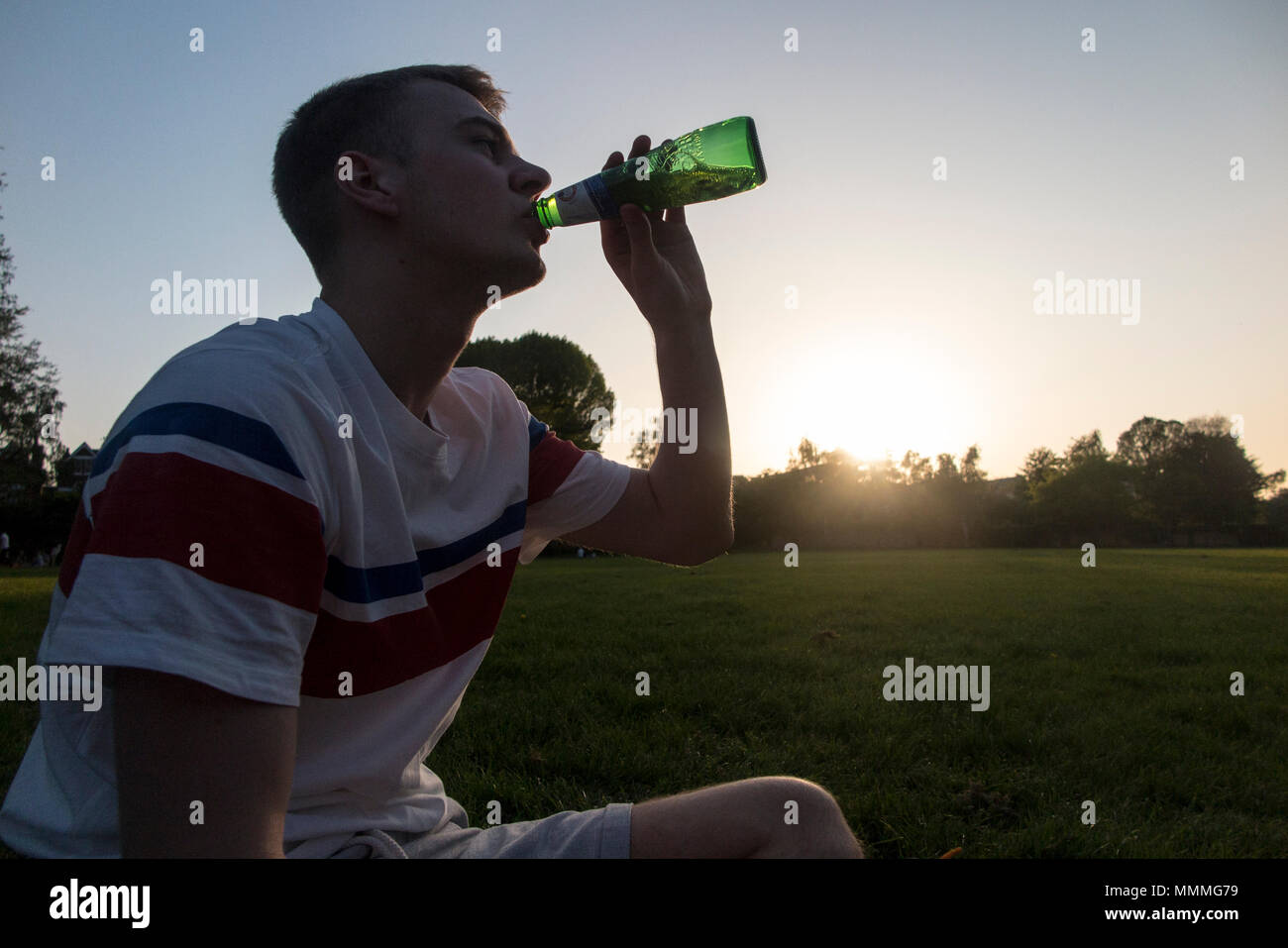 A mother and teenage son enjoy drinks in the evening as the sun sets in a London park Stock Photo