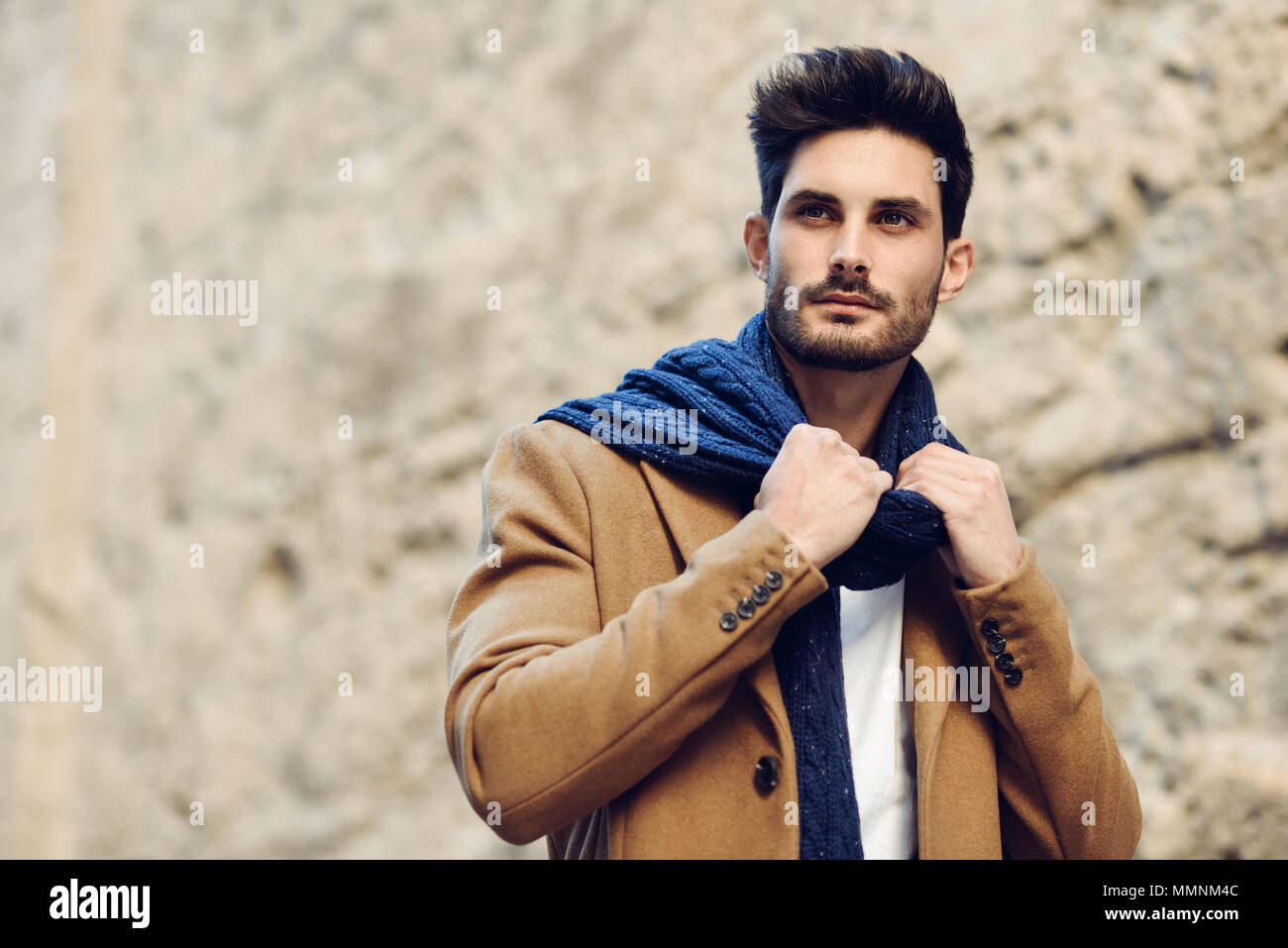 Young man wearing winter clothes in the street. Young bearded guy with  modern hairstyle with coat, scarf, blue jeans and t-shirt Stock Photo -  Alamy