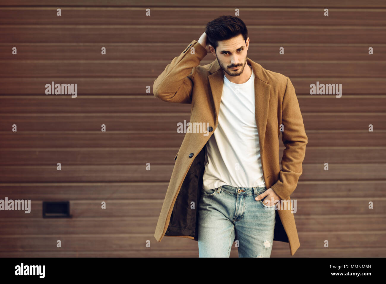 Young man wearing winter clothes in the street. Young bearded guy with  modern hairstyle with coat, blue jeans and white t-shirt Stock Photo - Alamy