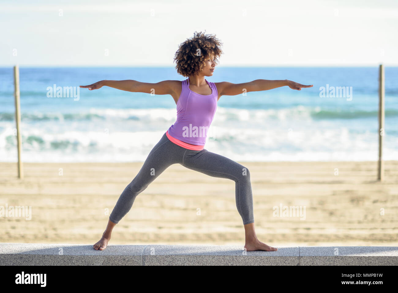 Black woman, afro hairstyle, doing yoga in warrior pose in the beach. Young  Female wearing sport clothes with sea at the background Stock Photo - Alamy