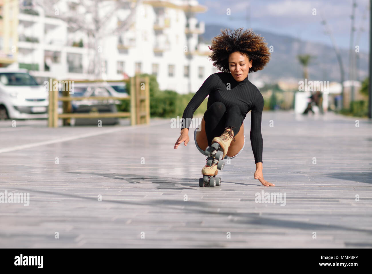 Young fit black woman on roller skates riding outdoors on urban street