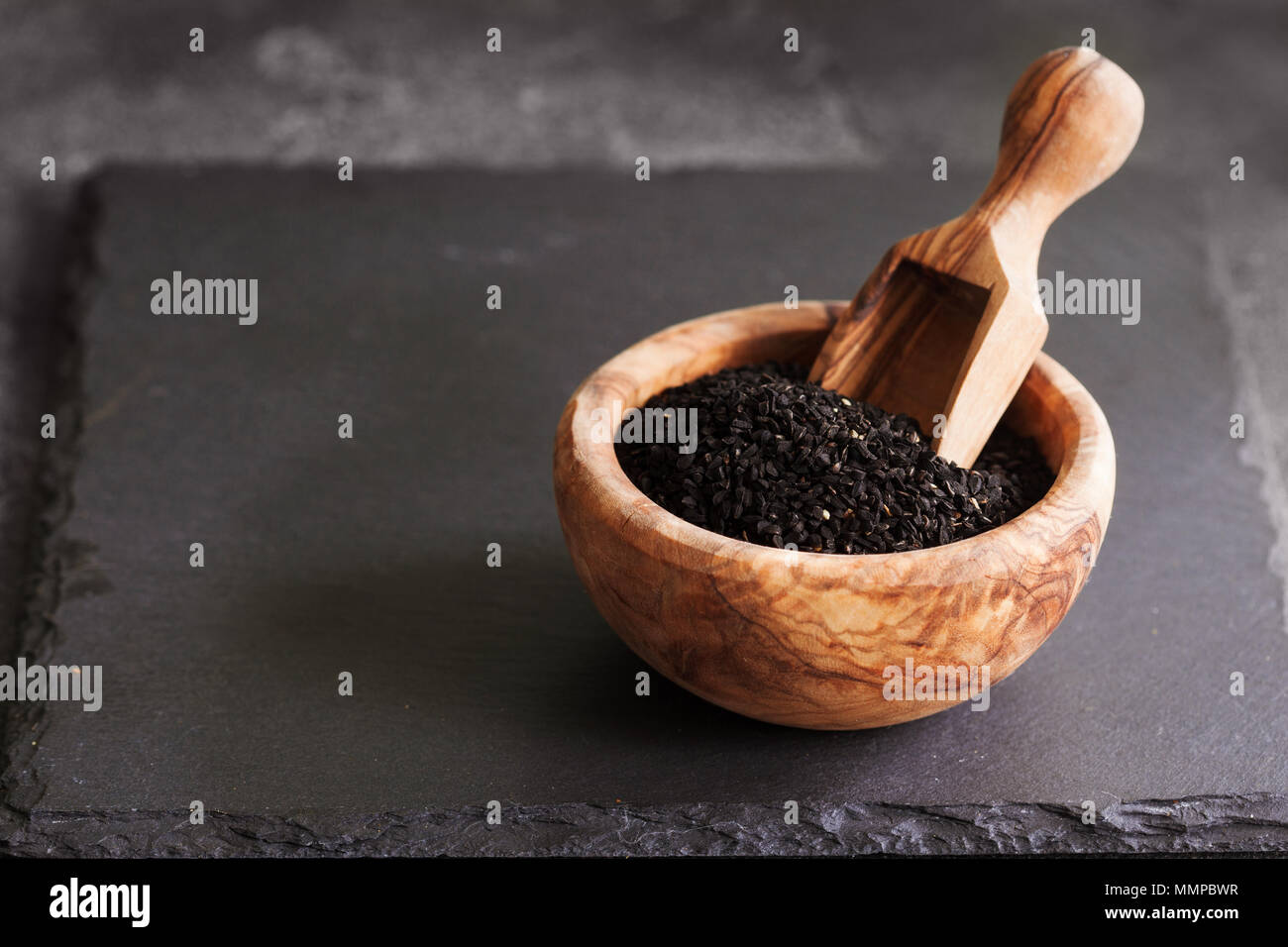 Black cumin or nigella sativa or kalonji seeds in bowl with spoon on black slate background, selective focus Stock Photo