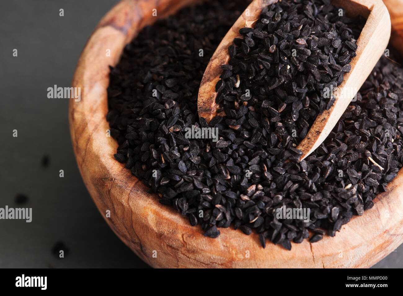 Black cumin or nigella sativa or kalonji seeds in bowl with spoon on black slate background, selective focus Stock Photo