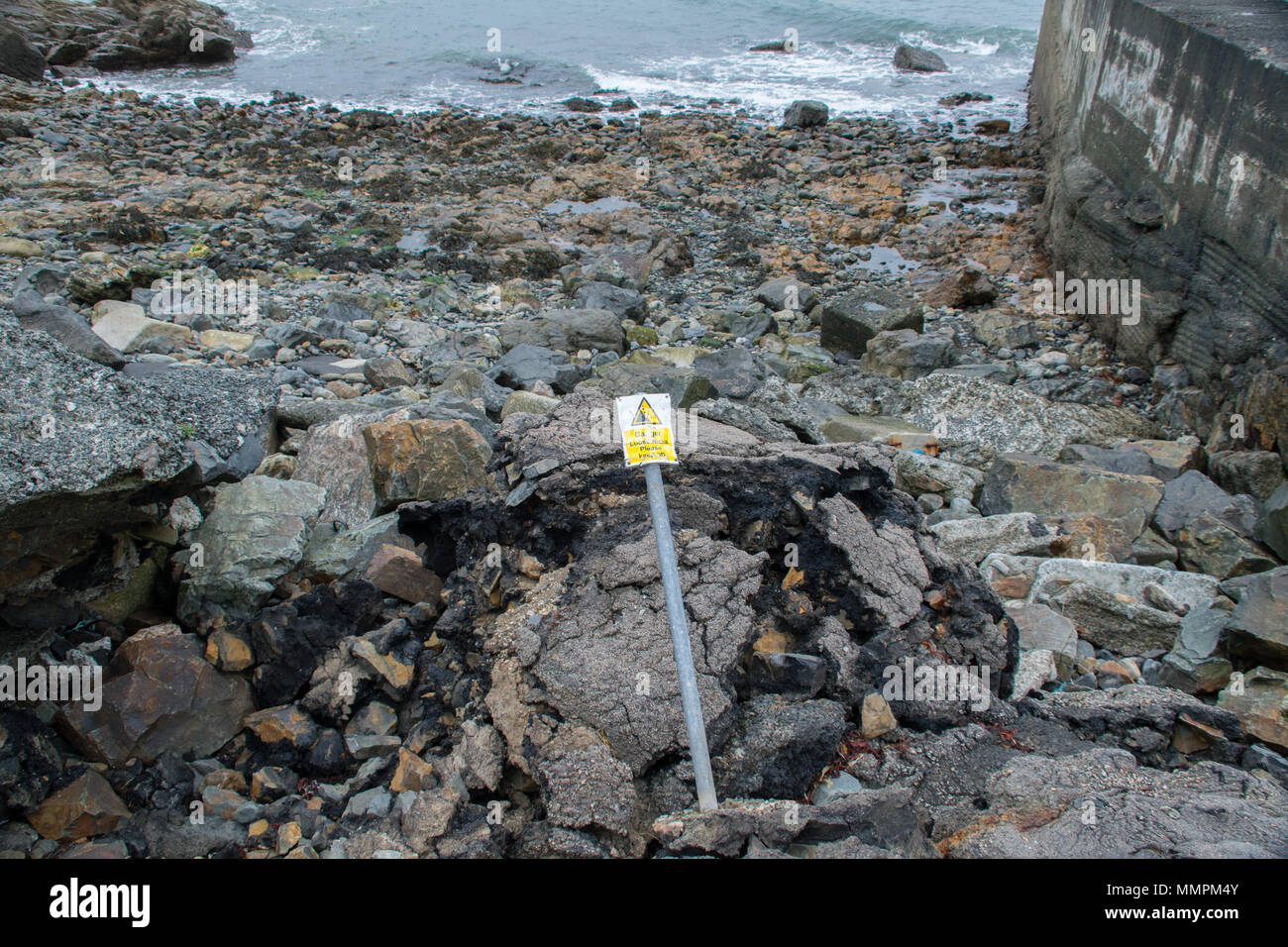 Danger loose rocks sign which has been bent and is falling over against some loose rocks on the coast at Newlyn in Cornwall Stock Photo