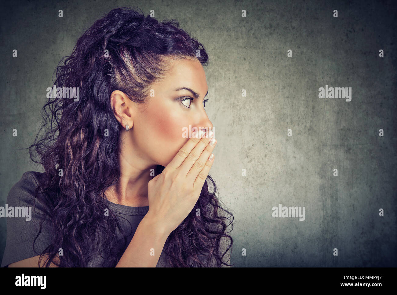 I have a secret to tell you. Woman whispering a gossip isolated on gray background Stock Photo