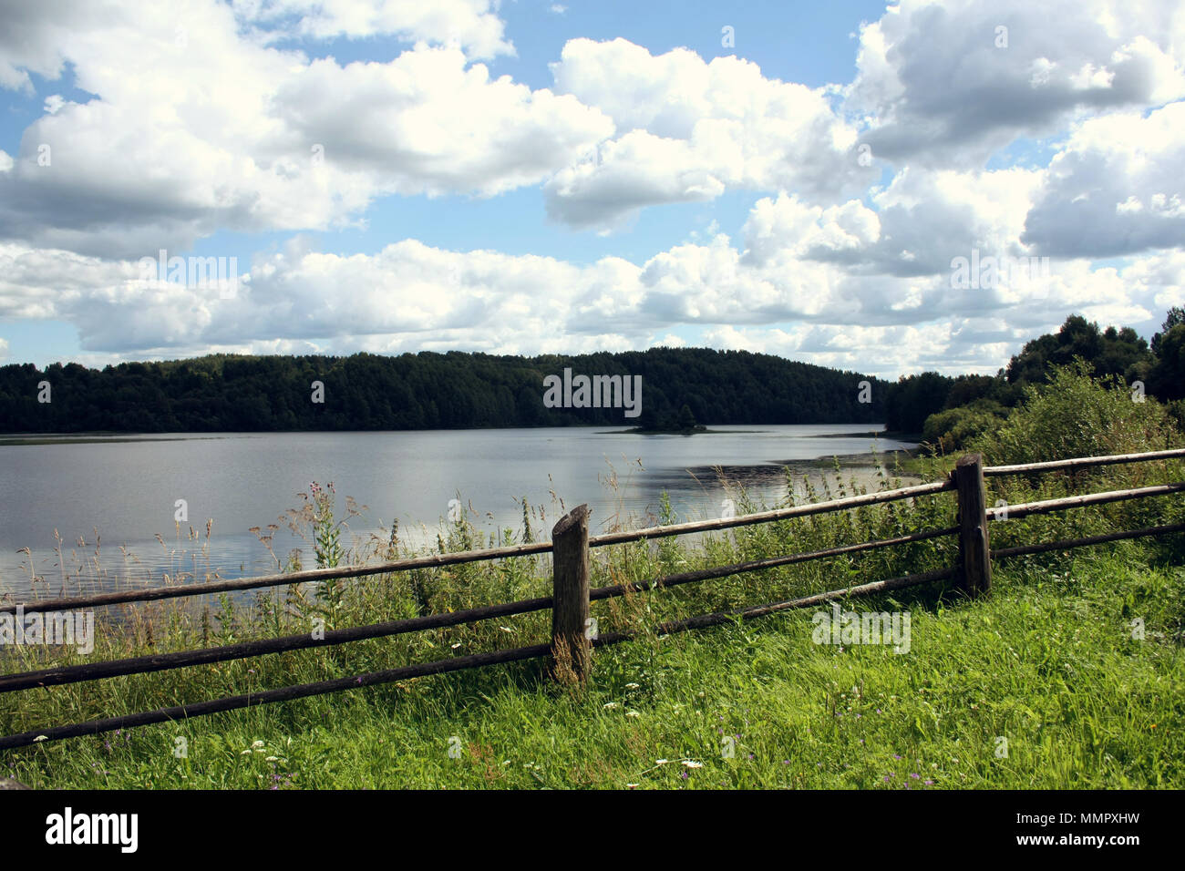 Wooden fence on the hill and view at Kenozero lake. Russian North countryside. Meadow and Grassland. Blue sky. Aged photo. Sunny summer day. Kenozersk Stock Photo
