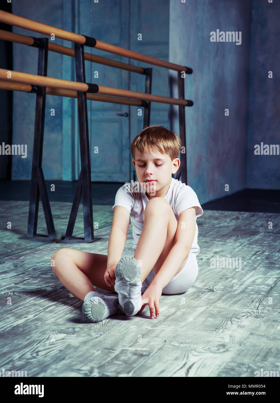 boy ballet dancer putting on pointes at dance class near the barre