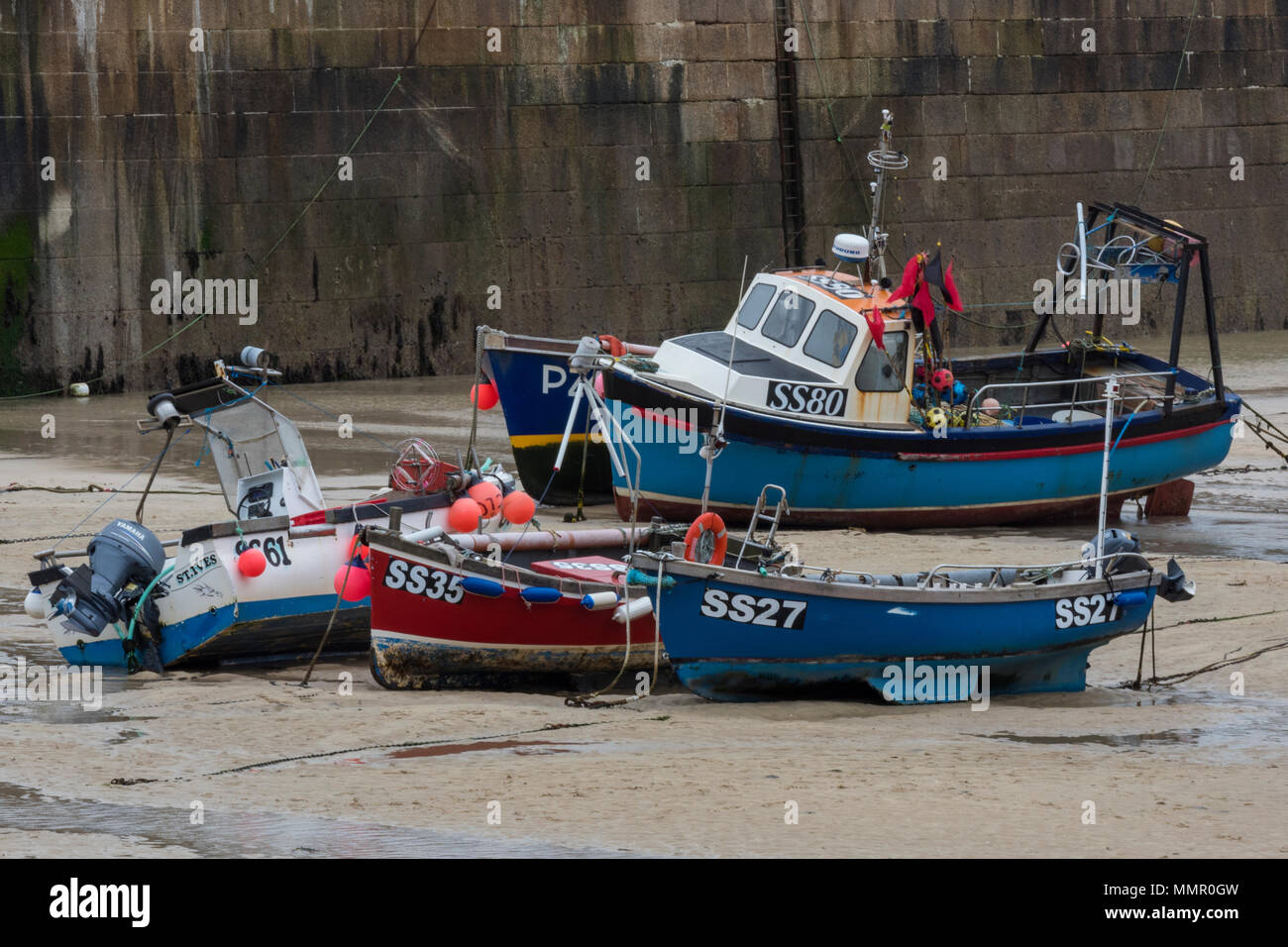 Traditional and colourful fishing boats on the sandy harbour in st Ives in cornwall high and dry at low tide. Inshore fishing craft beached on shore. Stock Photo