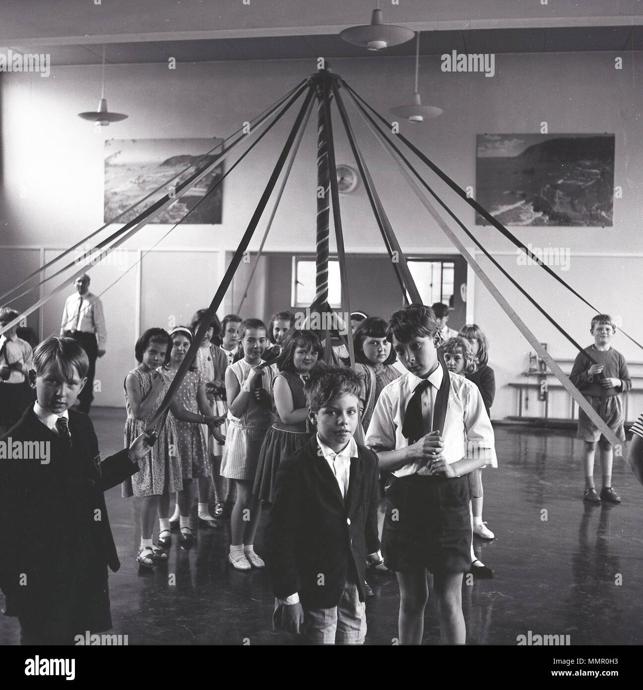1950s, group of school children in their hall gathered a maypole, holding the ribbons. This was a dancing activity, involving skipping and movement. Stock Photo