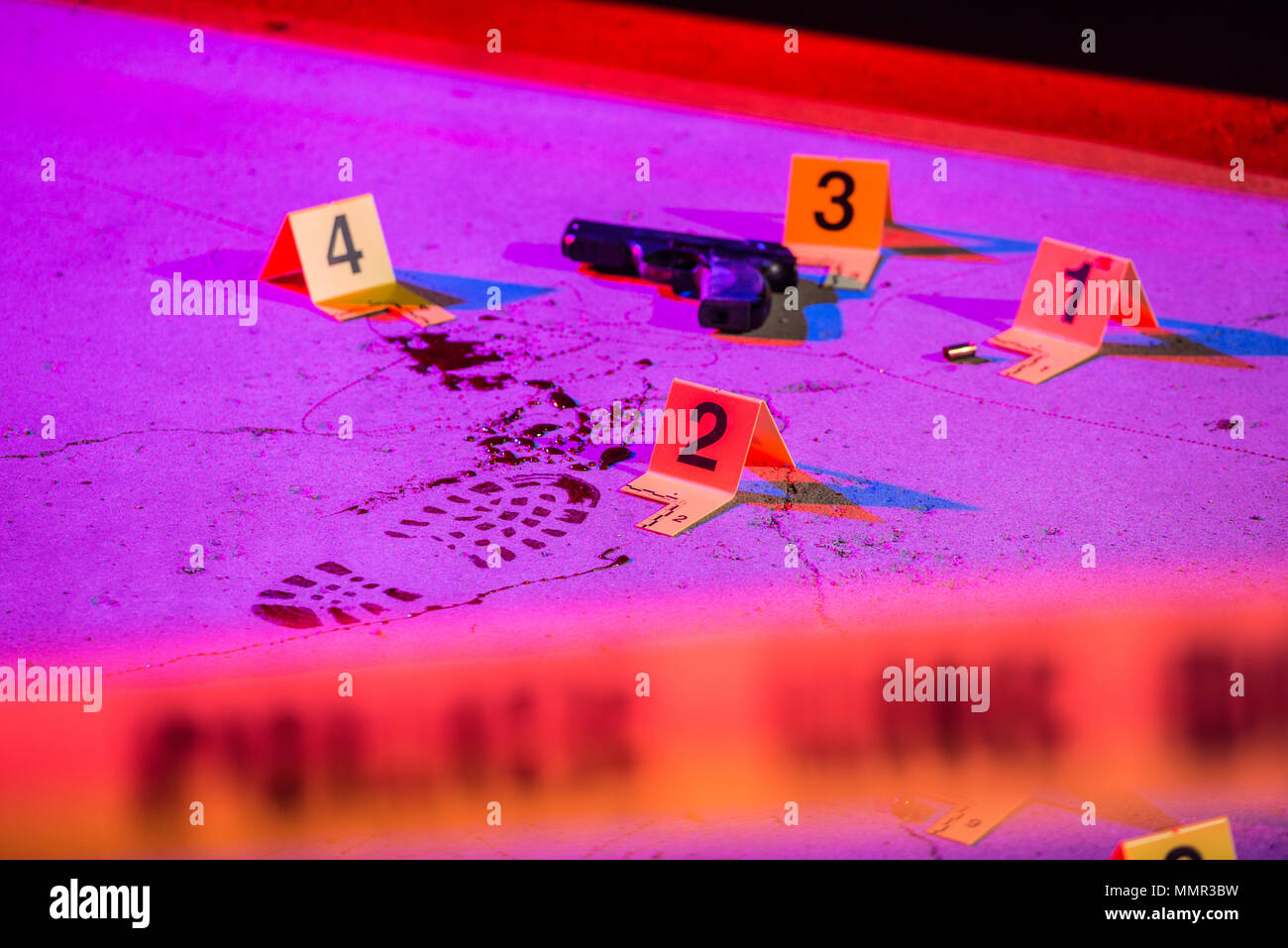 A bloody footprint and firearm are marked with evidence markers within a crime scene. Cordon tape can be seen in the foreground. Stock Photo
