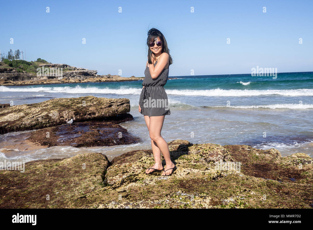 Young woman with sunglasses standing on the rocky shore of Maroubra beach, Sydney, Australia. Stock Photo