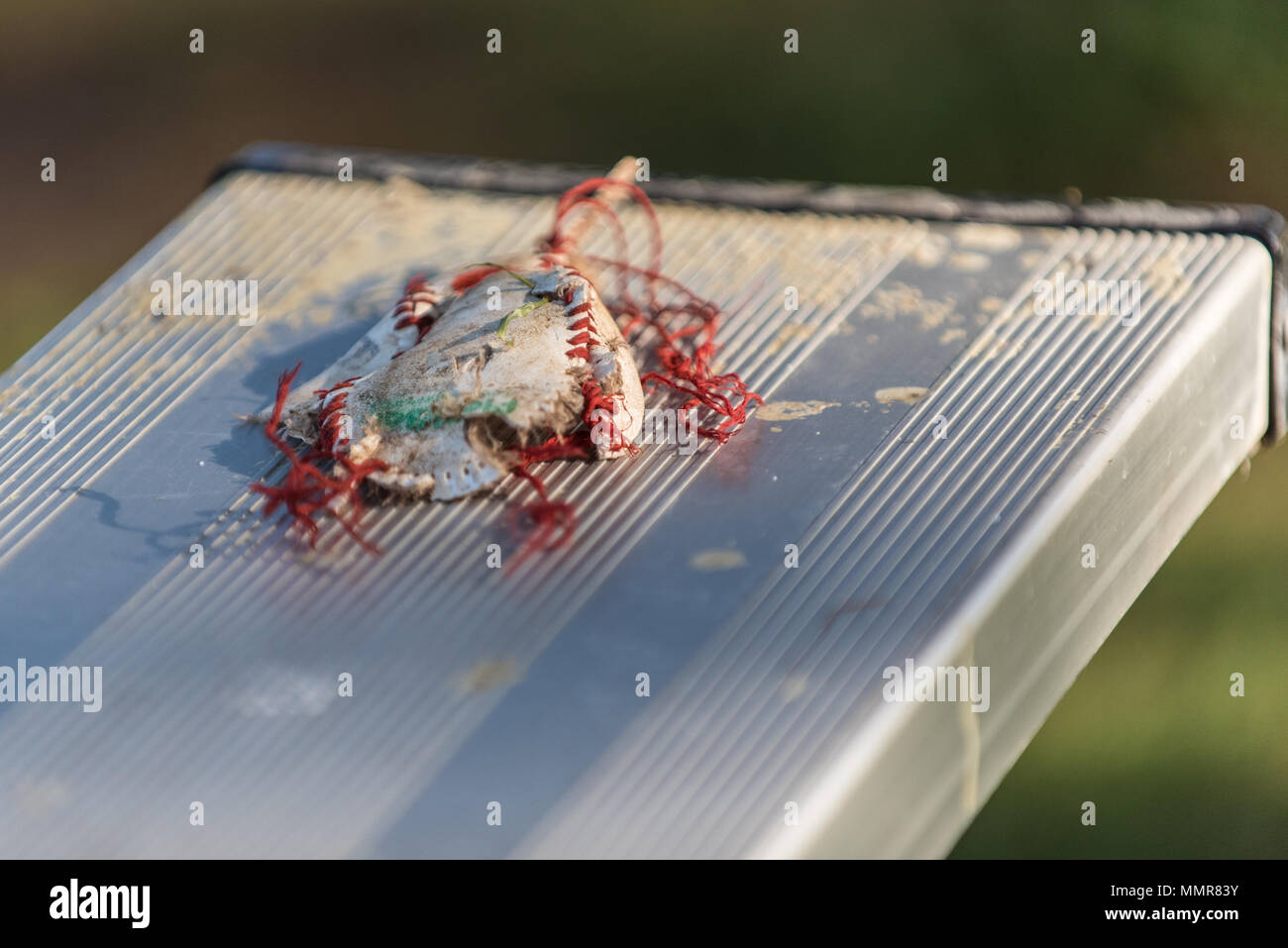 Baseball cover frayed, tattered, and smashed onto stadium bleacher