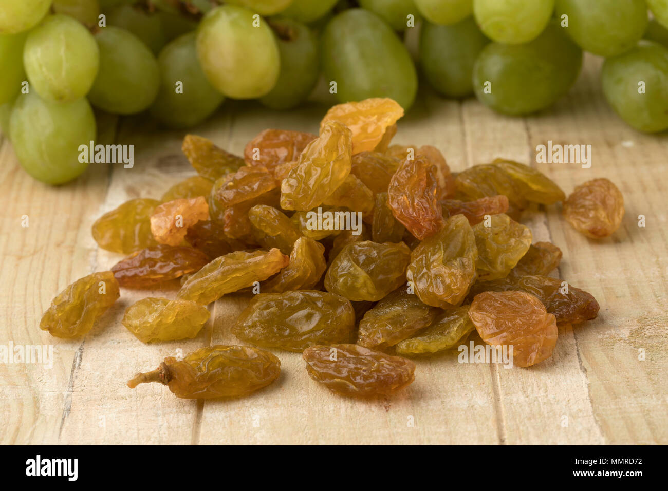 Heap of golden yellow jumbo raisins and fresh green grapes in the background Stock Photo