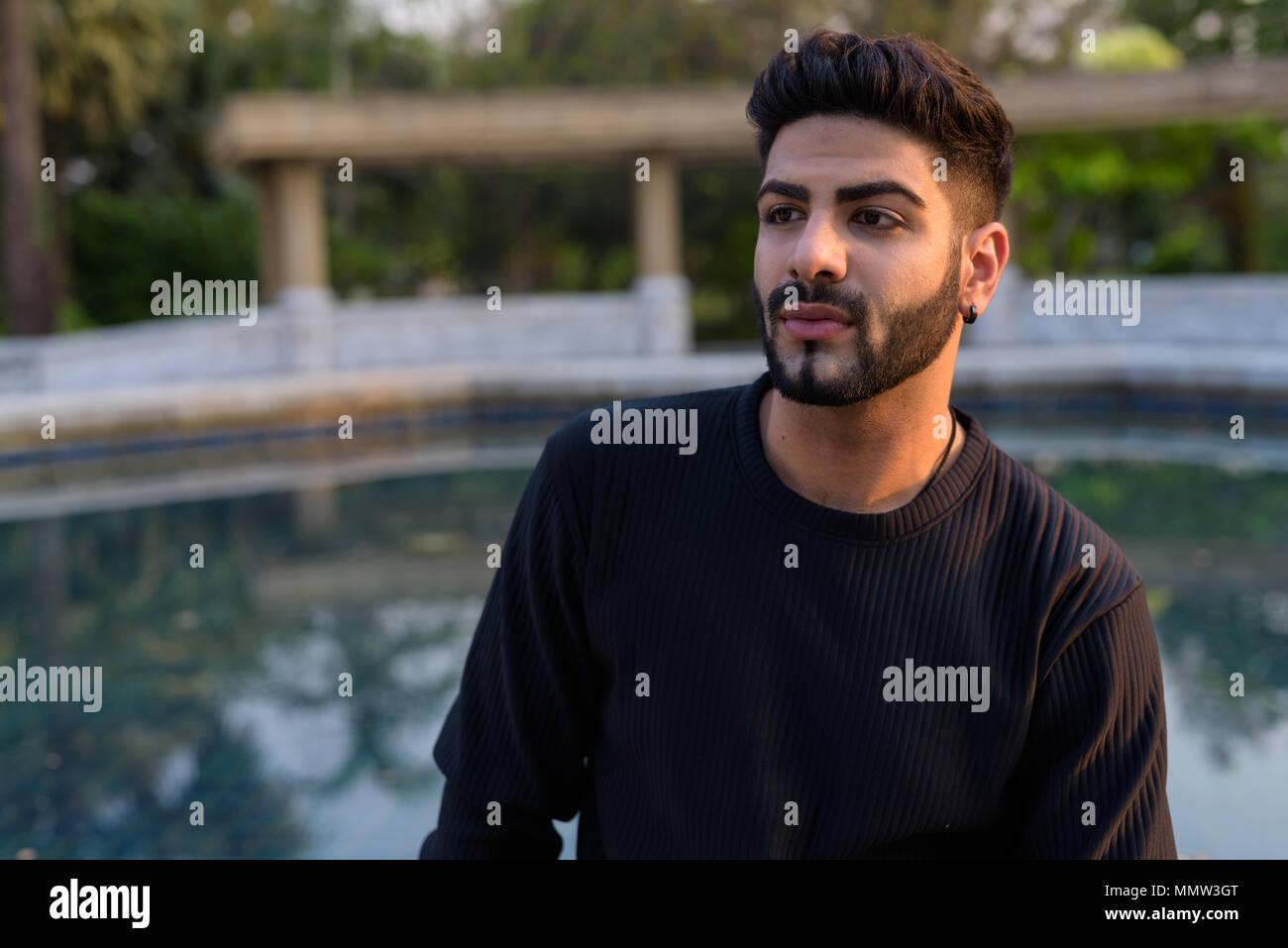 Young handsome Indian man thinking against view of old swimming  Stock Photo