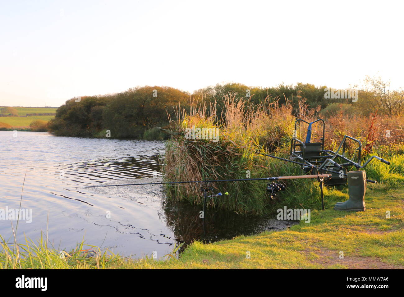 Fishing rods set up on lake with wellington boots at the ready Stock Photo