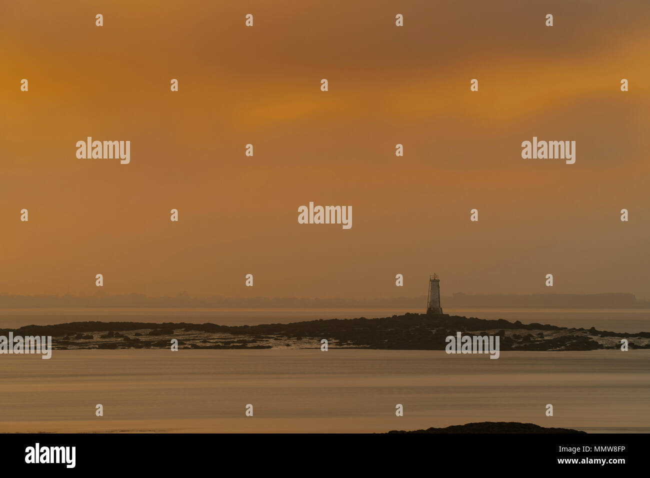 Image of lighthouse off the coast taken at sunrise. Morning glow. light, sky. Stock Photo