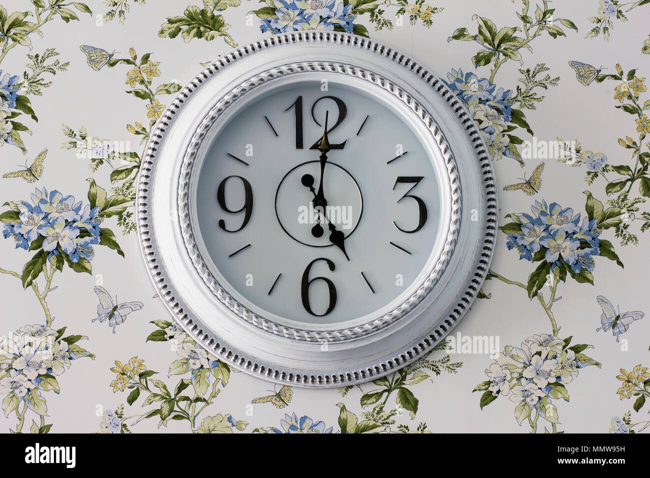 Round elegant white wall clock, five o'clock in the evening, interior