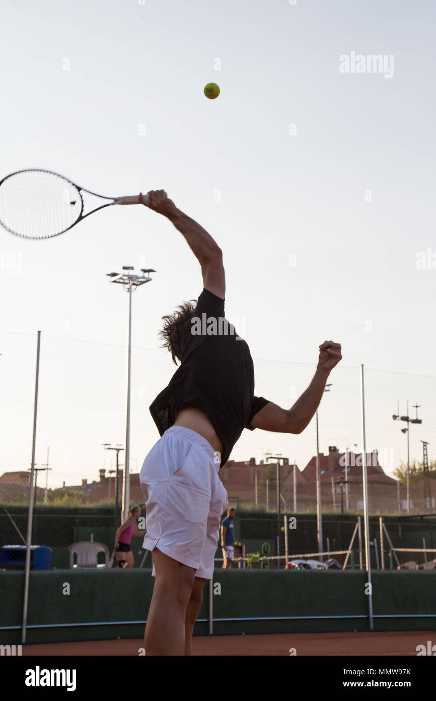 Back view of sportsman with tennis racket hitting ball in back light on