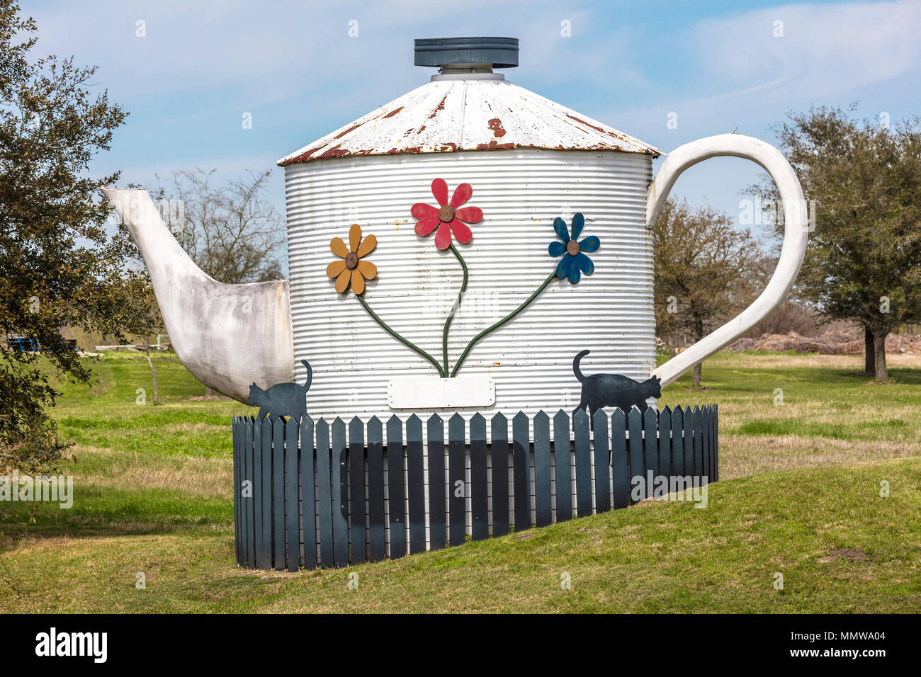 Oversized tea kettle with two black cats in front yard of Texas home